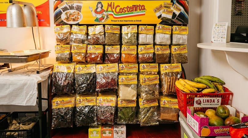 A display of Mi Costeñita spices and dried goods, with fresh bananas and mangoes nearby.